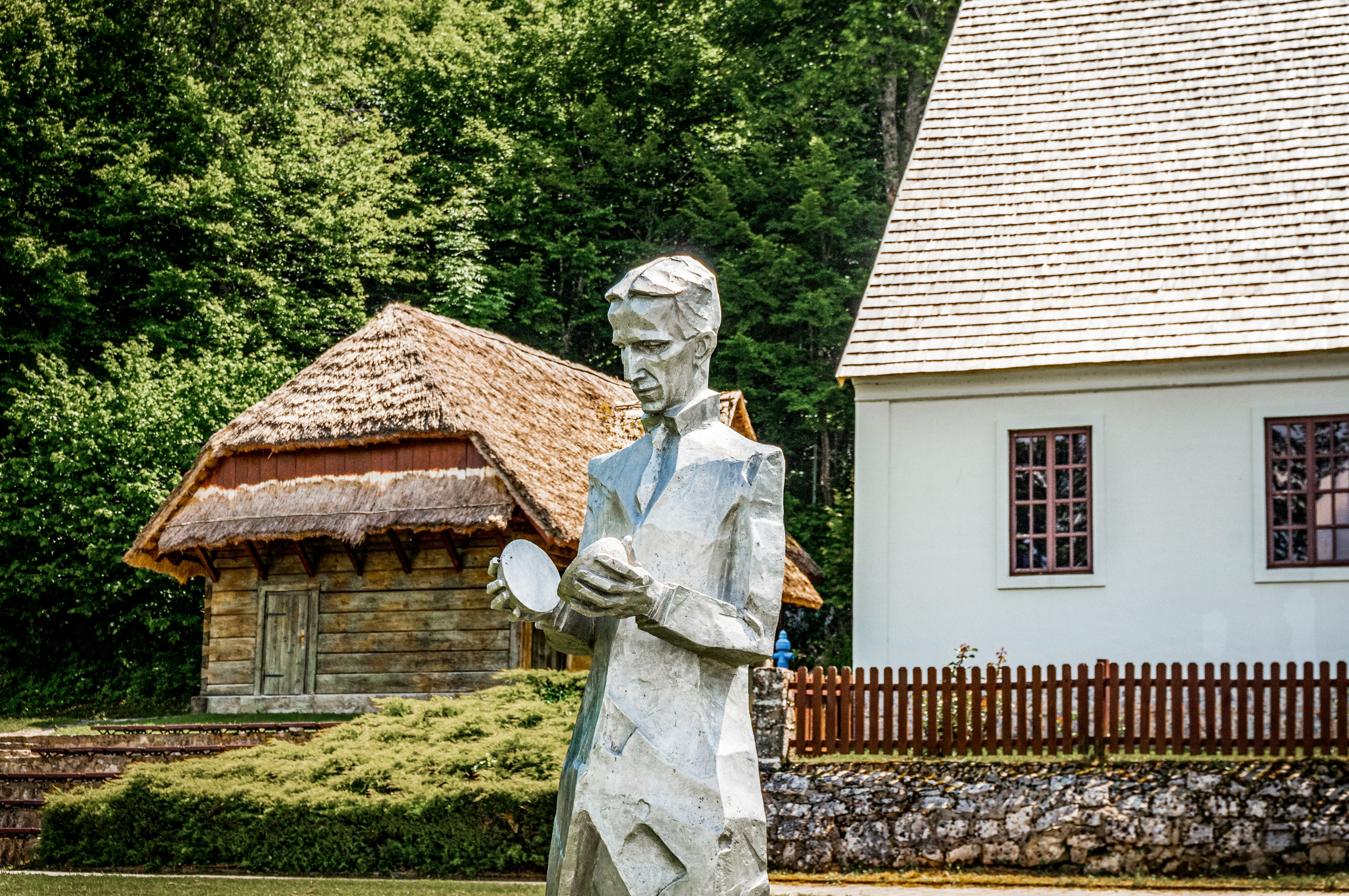 white concrete statue near brown wooden house during daytime